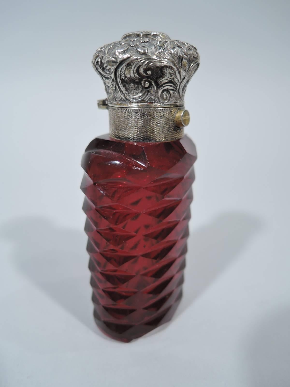 European silver and faceted ruby glass perfume, circa 1890. Ovoid with lozenge faceting. Silver collar with engine-turned wave ornament and hinged bun cover with worked flowers and applied cartouche (vacant). Glass is deep red. Unmarked.