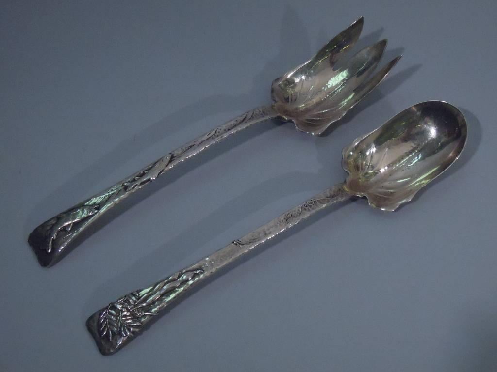 Sterling silver long-handled salad serving spoon and fork in lap over edge pattern. Made by Tiffany. all-over hand-hammering, a tapering handle, and applied ornament (fish and foliage on fork, foliage on spoon). The fork shank has a curvilinear bowl