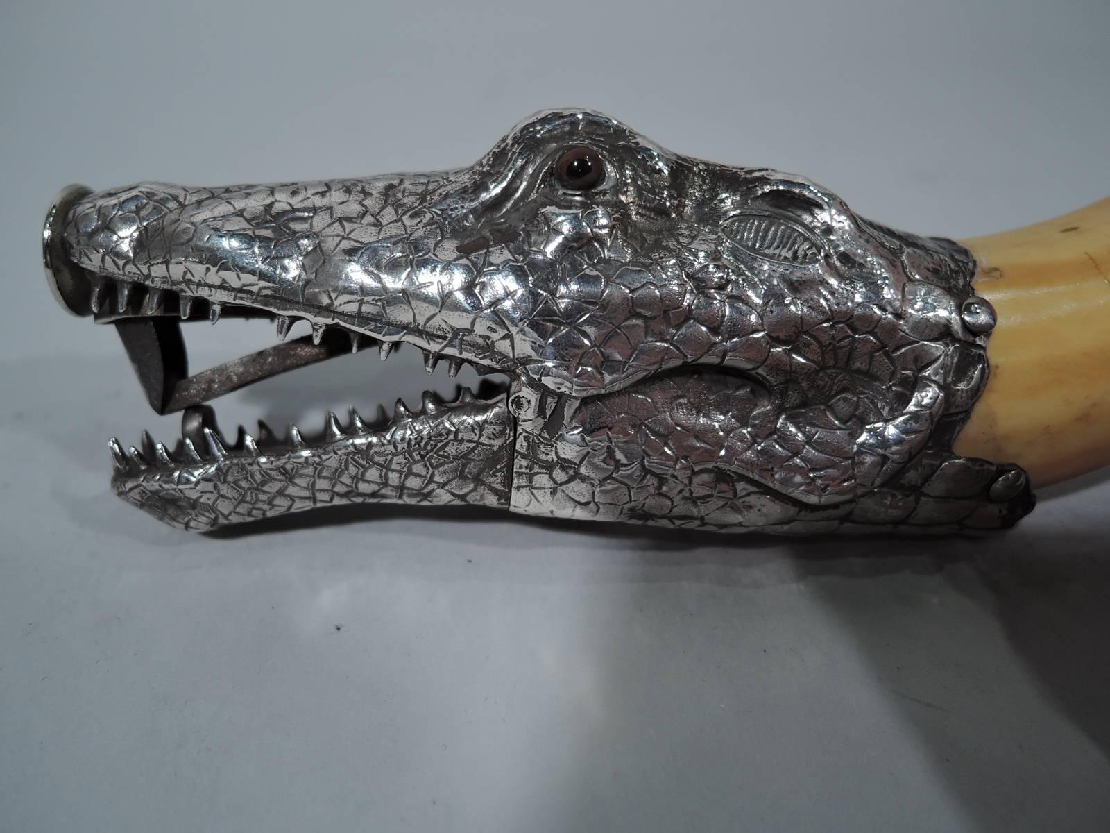Boar’s tusk cigar cutter with silver reptile mount, circa 1910. Mount in form of crocodile head with weathered and scaly hide and brown glass eyes. Blade concealed in mouth, which also has some major dentition. Snap go the jaws! European hallmark –