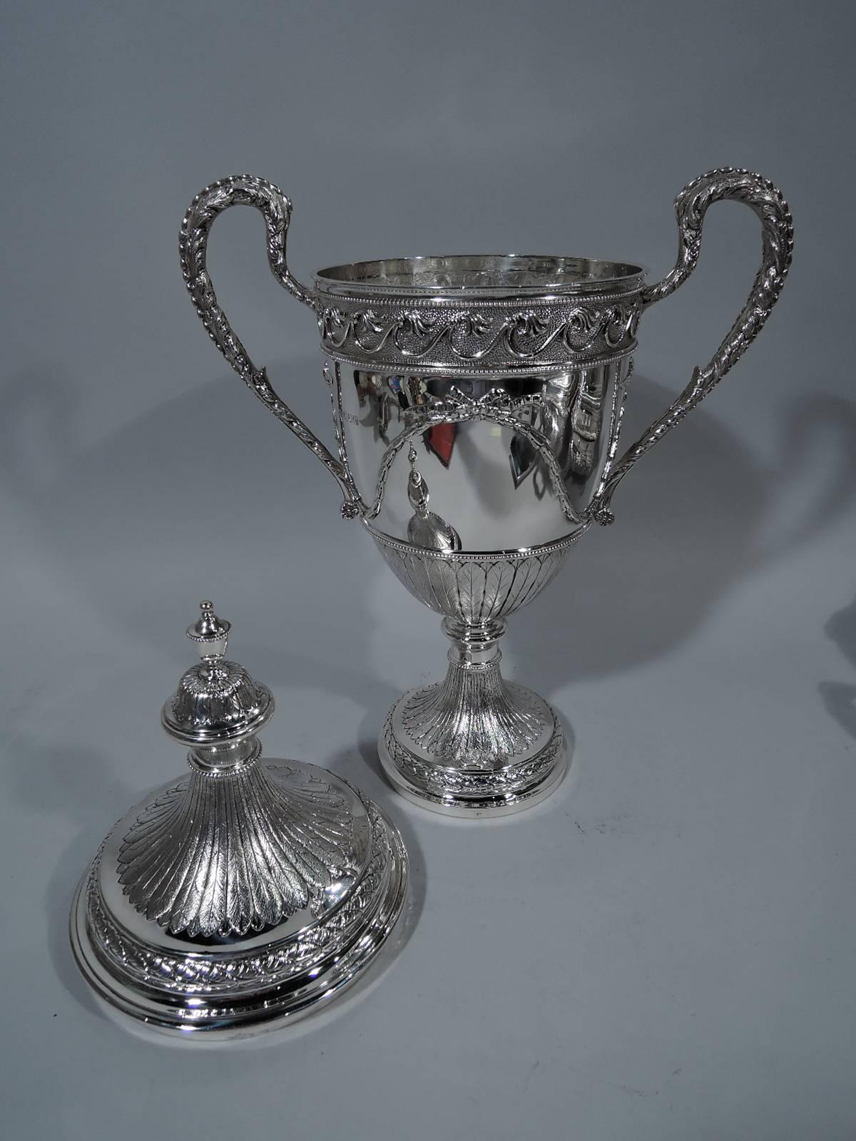 George V sterling silver trophy cup. Made by Goldsmiths & Silversmiths in London in 1912. Amphora with high-looping side handles and double-domed cover. Leaves, bow-tied garland, Vitruvian scroll, and beading. A neoclassical urn repeated in small