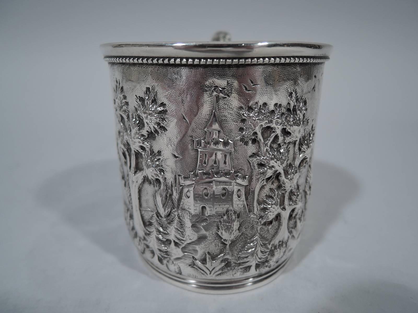 Sterling silver baby cup. Made by AG Schultz & Co. in Baltimore, circa 1900. Straight sides with foot ring, beaded rim, and worked scroll handle. Fanciful landscape with turreted bridge, castellated tower, and windmill. Sweet pastoral nostalgia.
