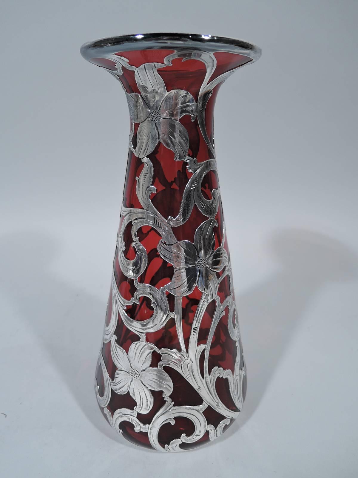 Art Nouveau glass vase with silver overlay. Made by Alvin in Providence, ca 1910. Conical with narrow mouth and flared rim. Silver scrolls and blossoms as well as asymmetrical cartouche with engraved script monogram. Lush flora on deep ruby red