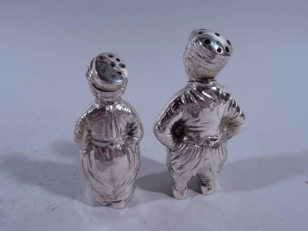 Pair of German 800 silver figural salt and pepper shakers, circa 1900. Two country children with firm stances and loose garments. Both wear pierced caps. One has detachable head. The other has detachable feet. Hallmarked. Nice condition and