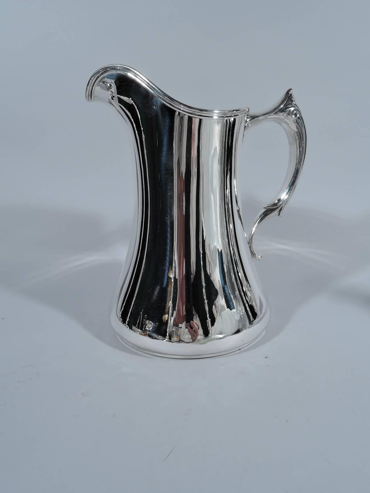 Stylish Edwardian sterling silver water pitcher. Made by Whiting in New York in 1906. Wide base and molded helmet mouth. Spare and functional with the fancy part limited to the feathery scrollwork that appears to melt into the handle. Hallmark