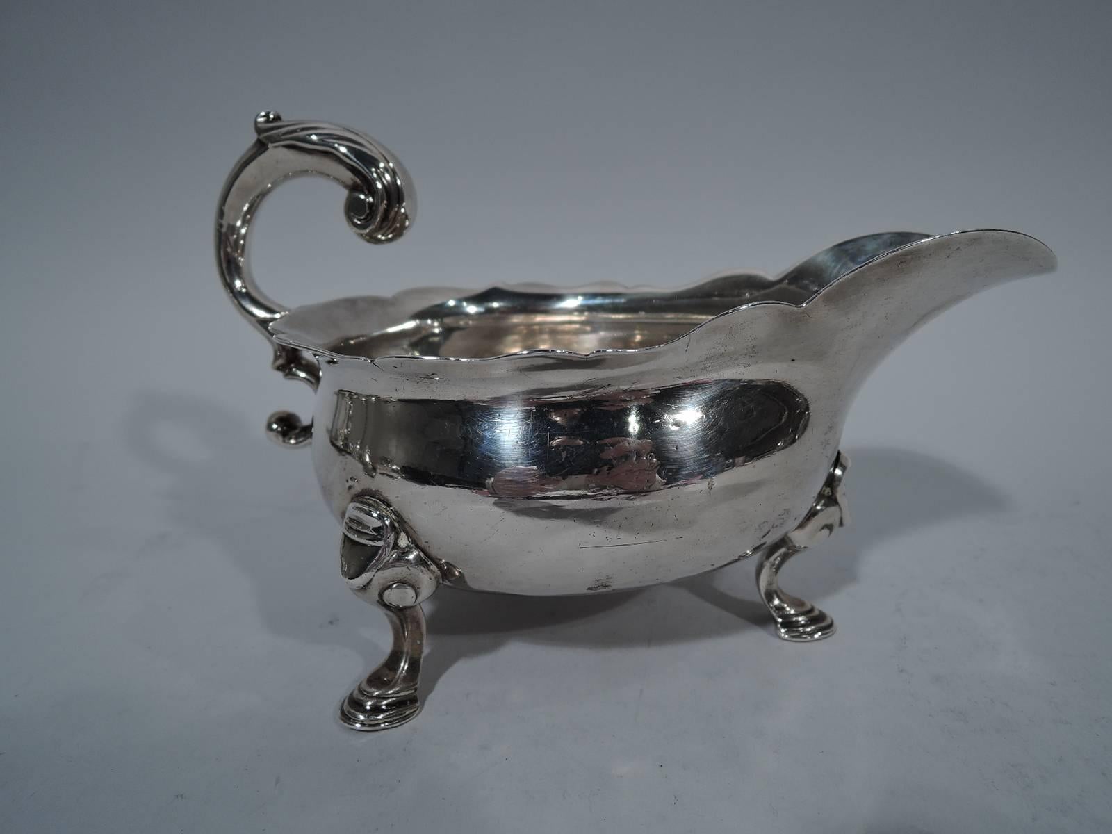George II sterling silver gravy boat. Bellied bowl with scrolled helmet mouth and leaf-capped double-scroll flying handle. Rests on 3 hoofs with volute scroll mounts. A great piece of sturdy, working Georgian. Worn hallmarks with London date letter