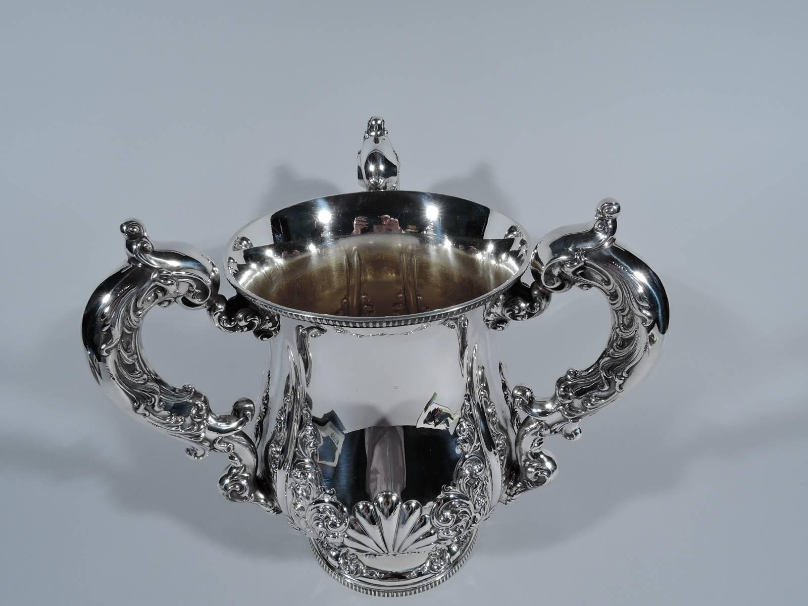 Fancy and heavy sterling silver trophy cup. Made by Frank W. Smith in Gardner, Mass, circa 1900. Baluster body with three leaf-capped scroll handles and raised foot. Repousse scallop shells at base with climbing scrolled leaves. Substantial ornament