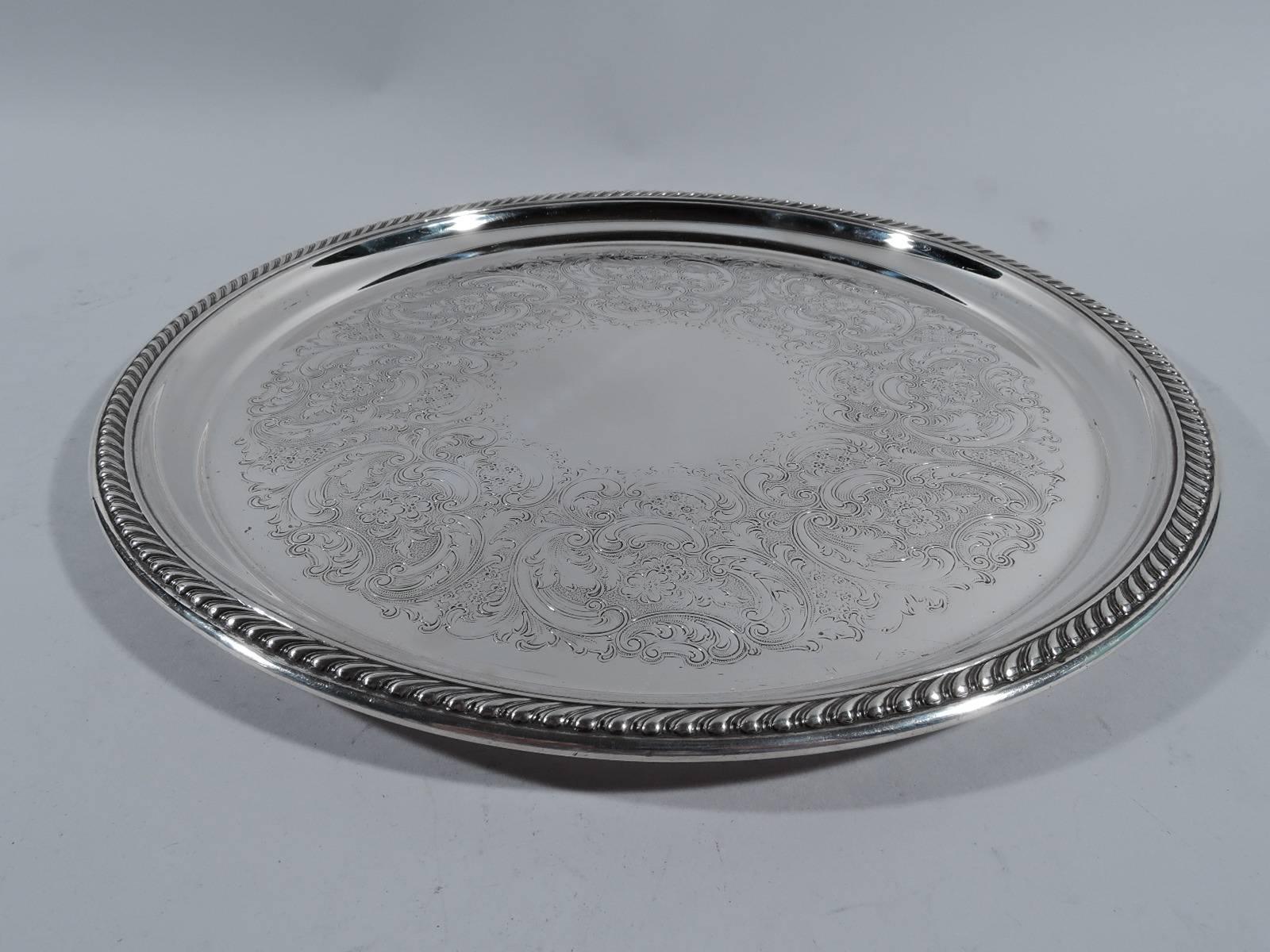 Traditional sterling silver serving tray. Made by Gorham in Providence. Circular with gadrooned rim. Vacant well center surrounded by dense scrollwork and flowers on stippled ground. Hallmark includes no. 42636. Heavy weight: 26.5 troy ounces.