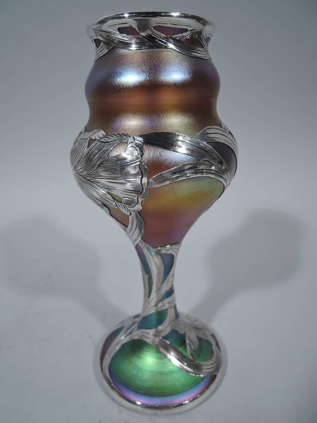 Fine quality art glass vase with silver overlay by historic New York maker Quezal, circa 1900. Fluid baluster bowl on stem on raised foot. Iridescent polychrome glass in shades of green, yellow, purple, and blue overlaid in silver with lush blossoms