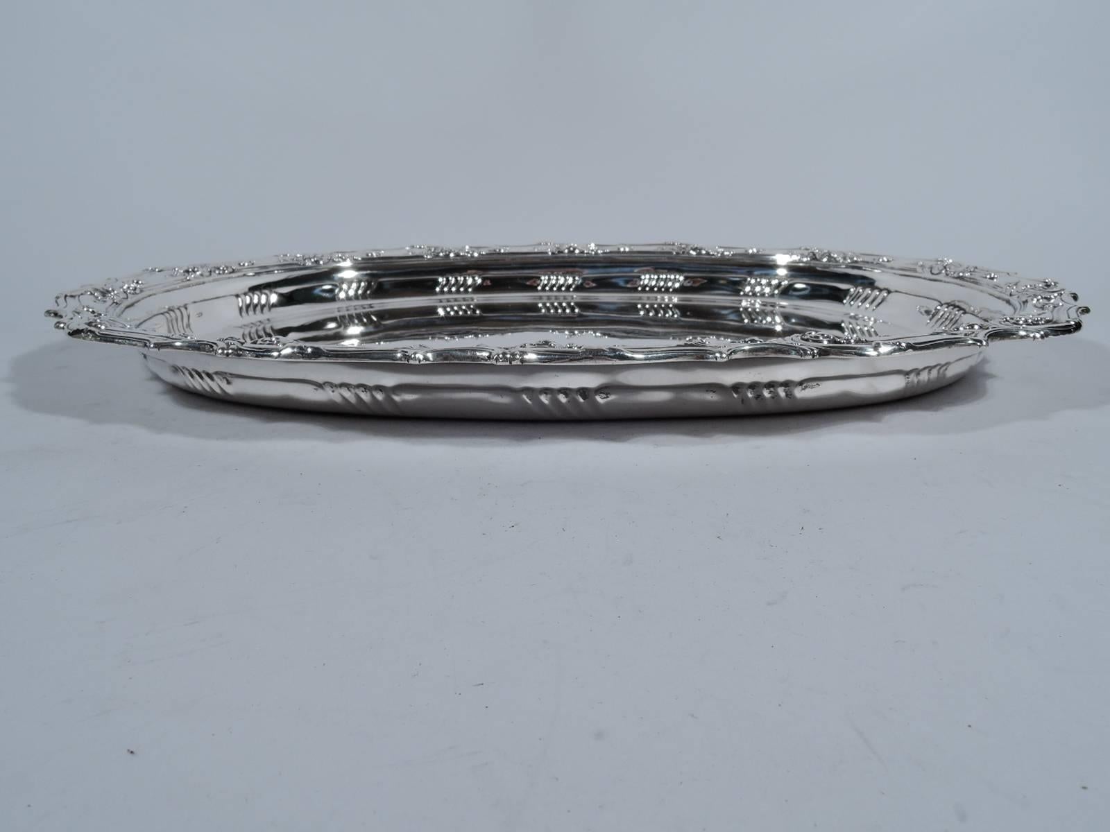 Antique sterling silver serving tray. Made by Tiffany & Co. in New York. Plain oval well tapering sides with slash lobing on interior, and everted rim with raised scrolls and flowers. Hallmark includes pattern no. 10617 and director’s letter T