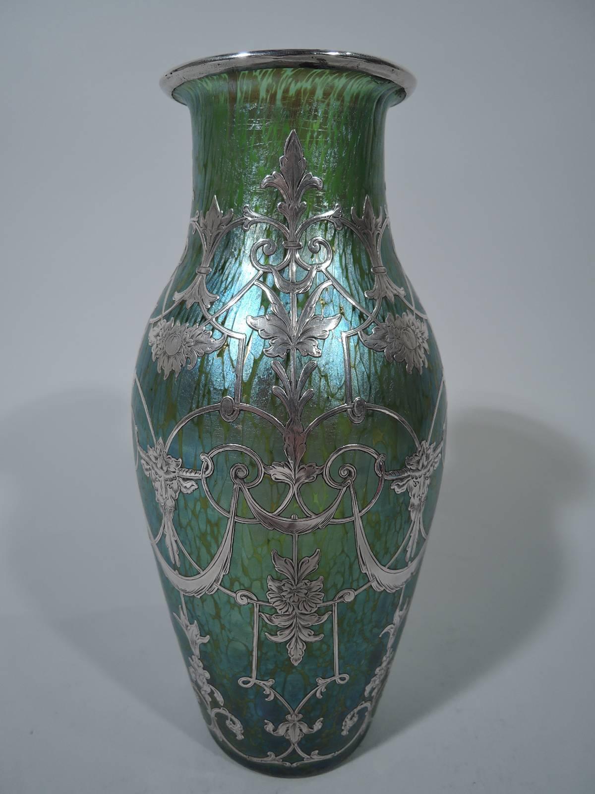 Art glass vase with silver overlay by historic Czech maker Loetz, circa 1900. Baluster with short neck and flat rim. Glass is green with irregular iridescence, and contrasts with the pretty and controlled silver overlay ornament in form of rondeaux,