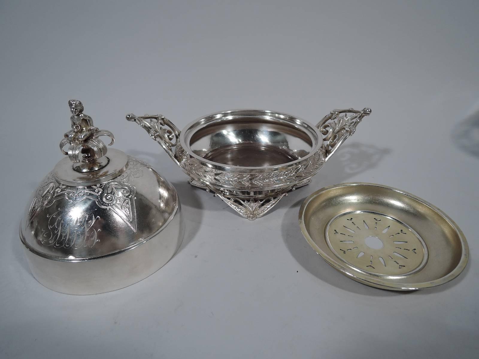 Aesthetic sterling silver butter dish. Made by Wood & Hughes (later Graff, Washbourne & Dunn) in New York, circa 1870. Bowl has tapering sides, turned-down rim, and four open triangular supports and two trefoil side handles inset with leaves. Domed