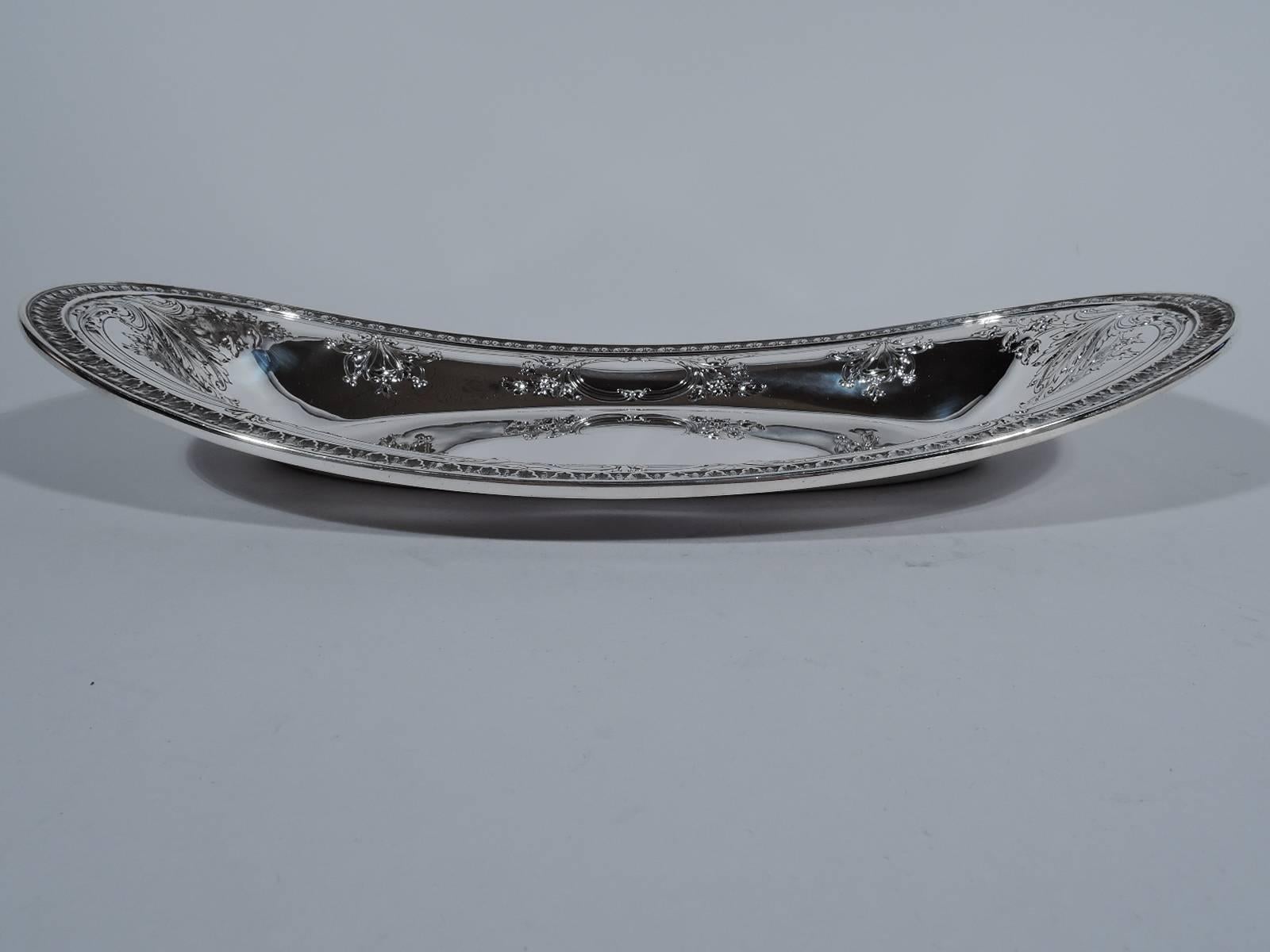 Fancy Edwardian sterling silver bread tray. Made by Gorham in Providence in 1919. Plain oval well, tapering sides, and swooping rim. Chased and repousse foliage and flowers as well as two oval frames (vacant). Leaf-and-dart rim. Hallmark includes