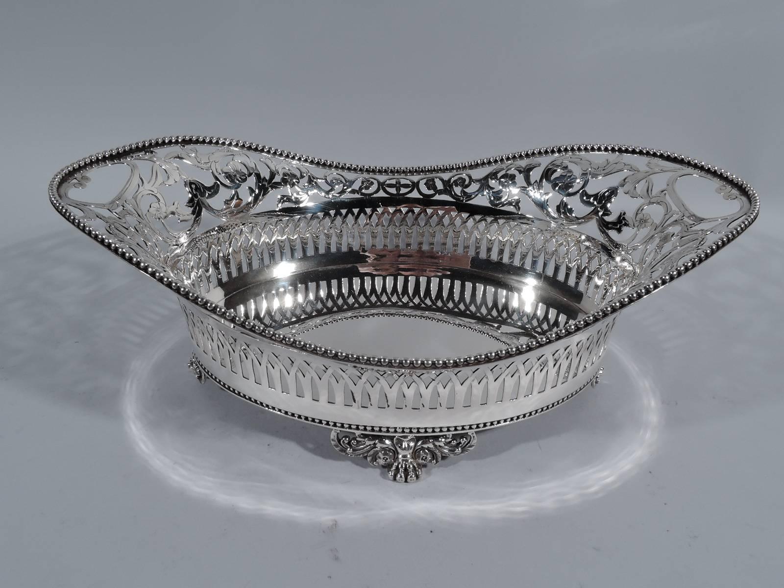 Sterling silver basket bowl. Made by Tiffany & Co. in New York, circa 1884. Solid well and pierced ornament: arcade surmounted by floral scrollwork and open end-handles. Beaded rim and base. Rests on four paw supports with pierced leaf mounts.