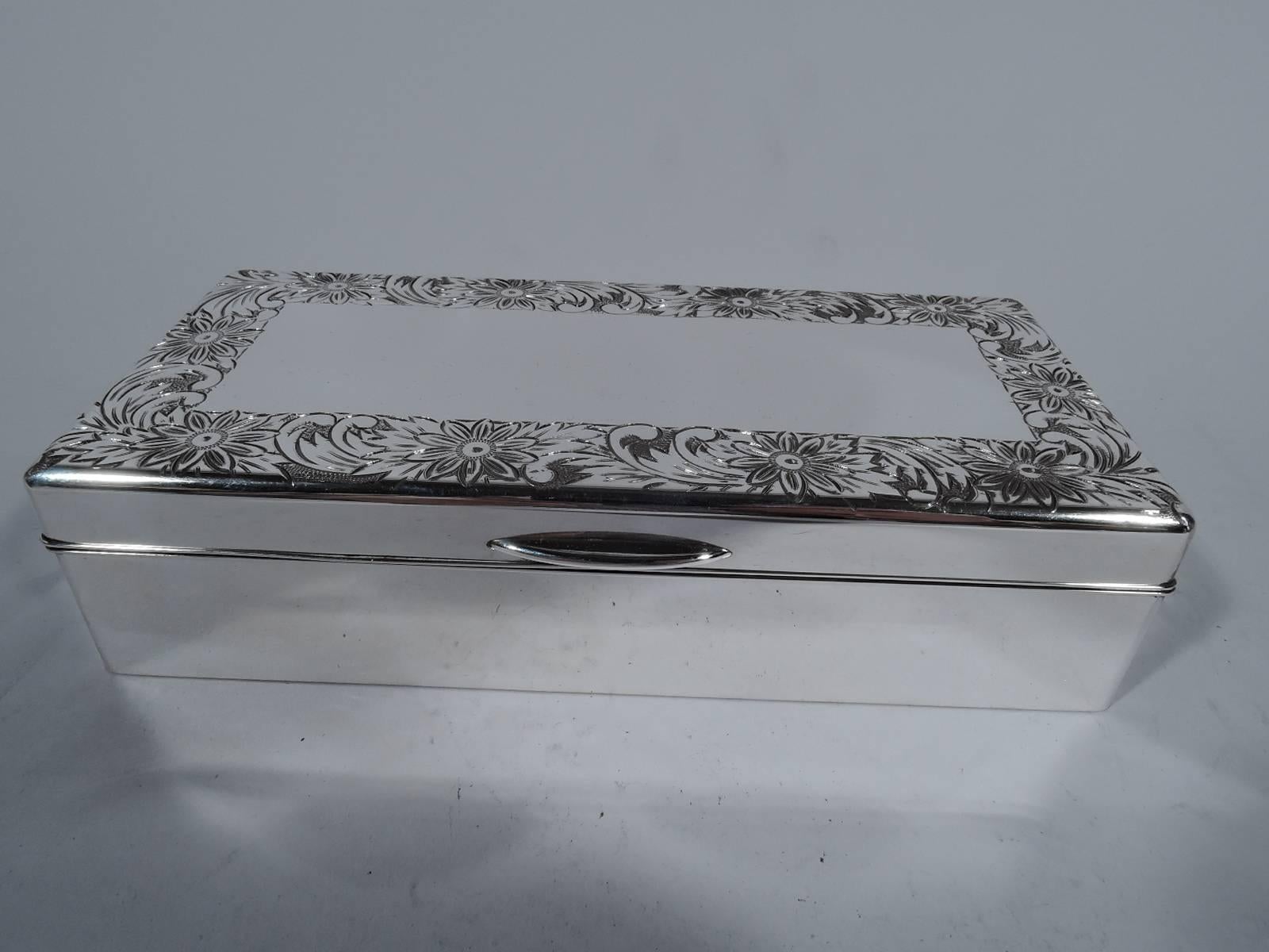 Lovely sterling silver keepsake box. Rectangular with straight sides. Cover hinged and tabbed. Cover top has engraved border with dense and overlapping flowers and leaves. Stained-wood bottom, lining, and partition. Cover interior has rectangular