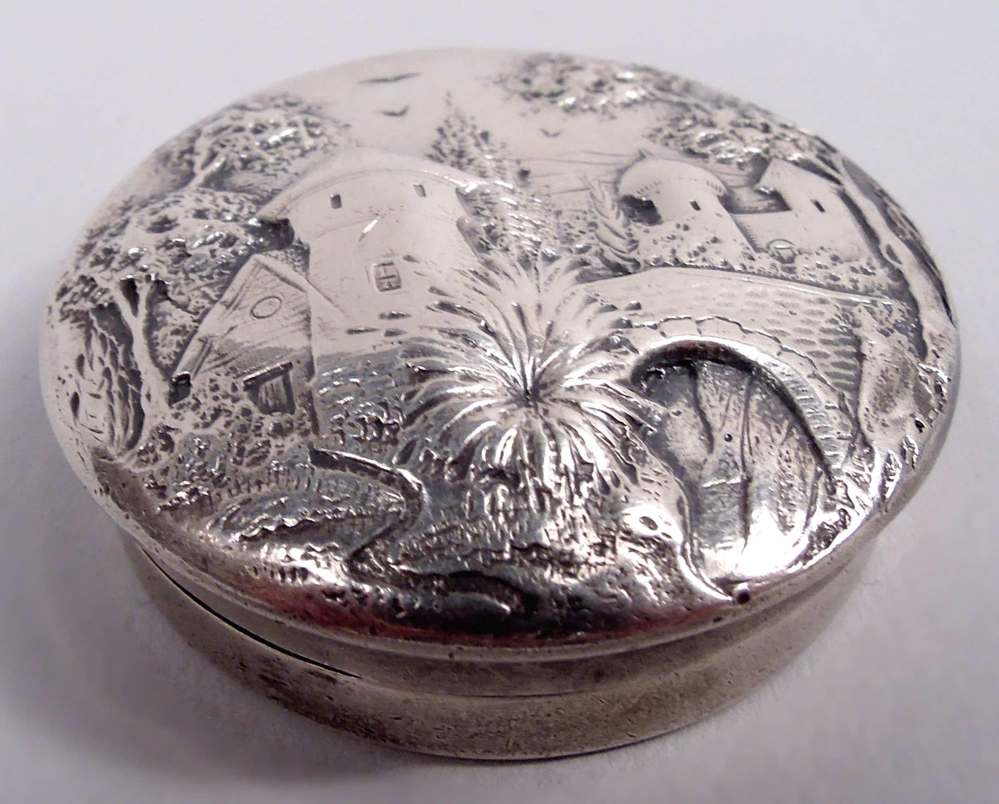 Edwardian sterling silver pillbox. Made by S. Kirk & Son Co. in Baltimore, ca 1910. Round with straight sides. Cover raised and overhanging with pictorial pastoral scene: Turrets and bridge in bosky surround. Fully marked including maker’s stamp
