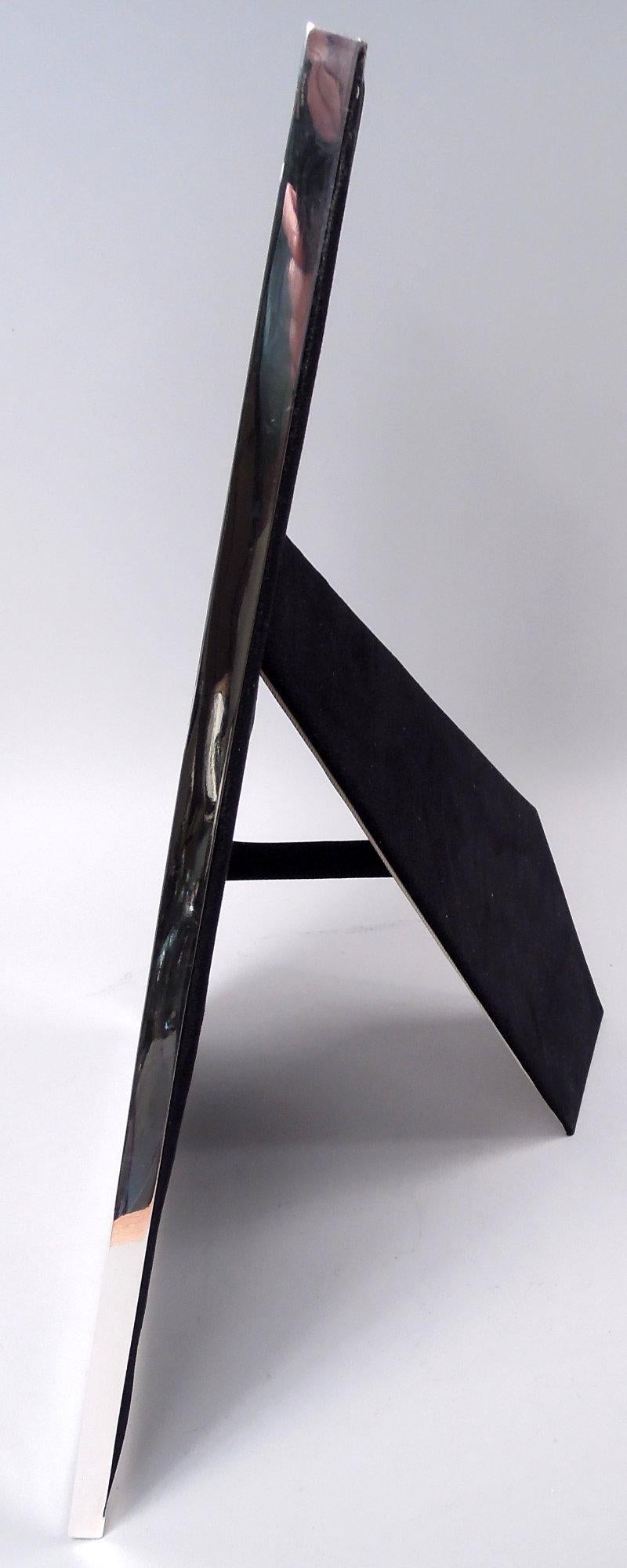 Cornice in argento sterling George V. Prodotto da Asprey London nel 1916. Bordo rettangolare piatto e liscio. Con vetro, fodera in seta, dorso in velluto e supporto a cavalletto incernierato per l'esposizione in verticale o in orizzontale.