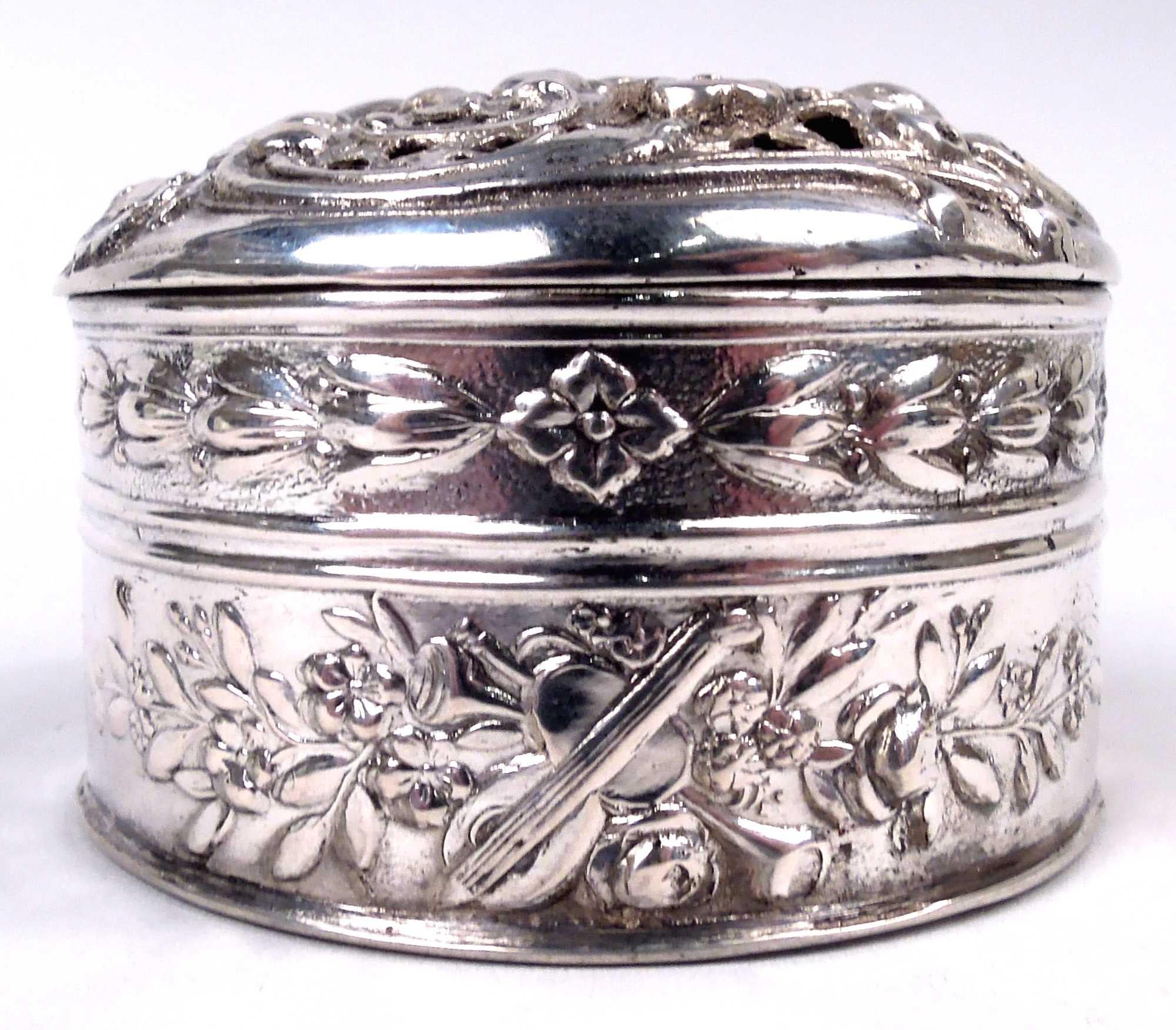 German Rococo 800 silver box, ca 1910. Round with straight sides; chased garland with musical trophies and imbricated bud and flowerhead band. Cover hinged and raised with cherub frolics and pierced scrollwork and flowers. Gilt-washed interior.