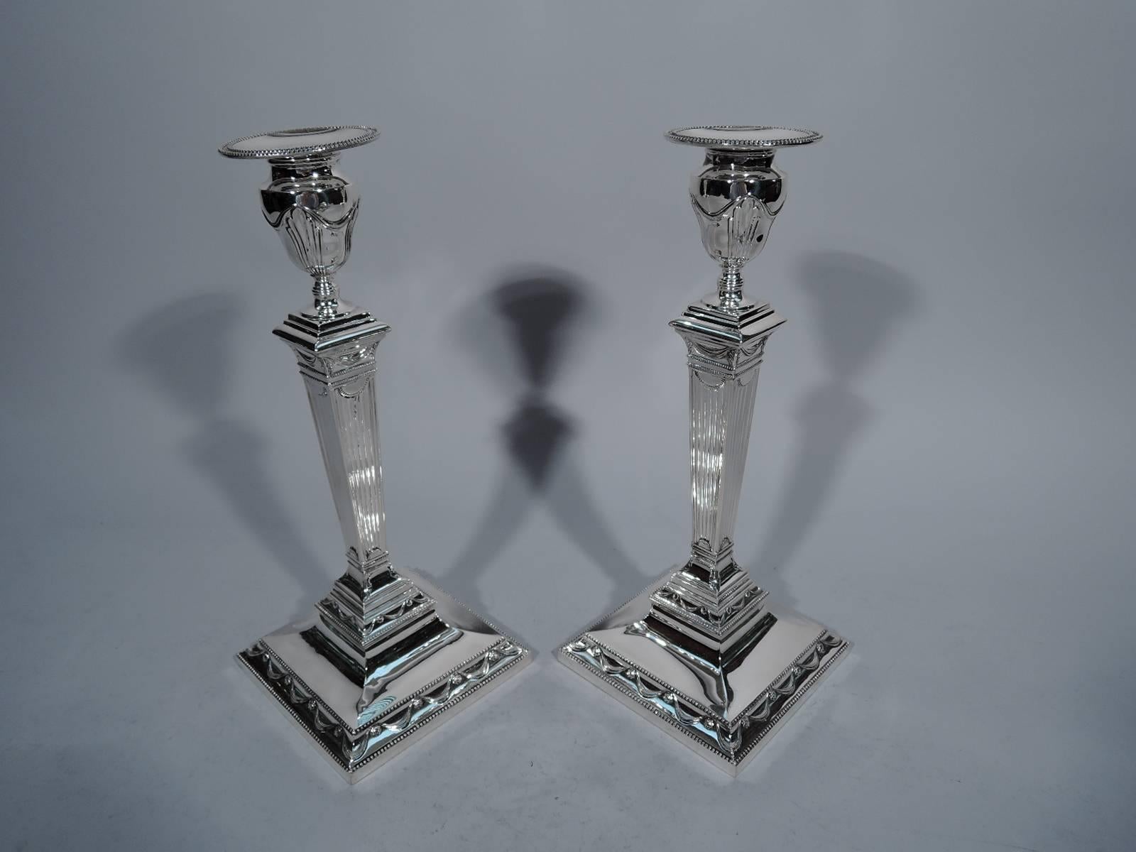 Pair of neoclassical sterling silver candlesticks. Made by Tiffany & Co. in New York, circa 1930. Tapering and reeded pillar on stepped square base. Urn socket with detachable bobeche. Beading, swags, and rosettes. The pattern (no. 21517) was first