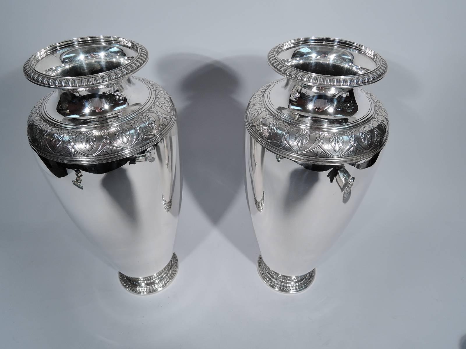 Pair of sterling silver vases. Made by Tiffany & Co. in New York, ca 1920. Each: baluster with curved shoulder, spread foot, short neck, and flared rim. Body and neck plain with contrasting stylized ornament: Classical leaf-and-dart on foot and