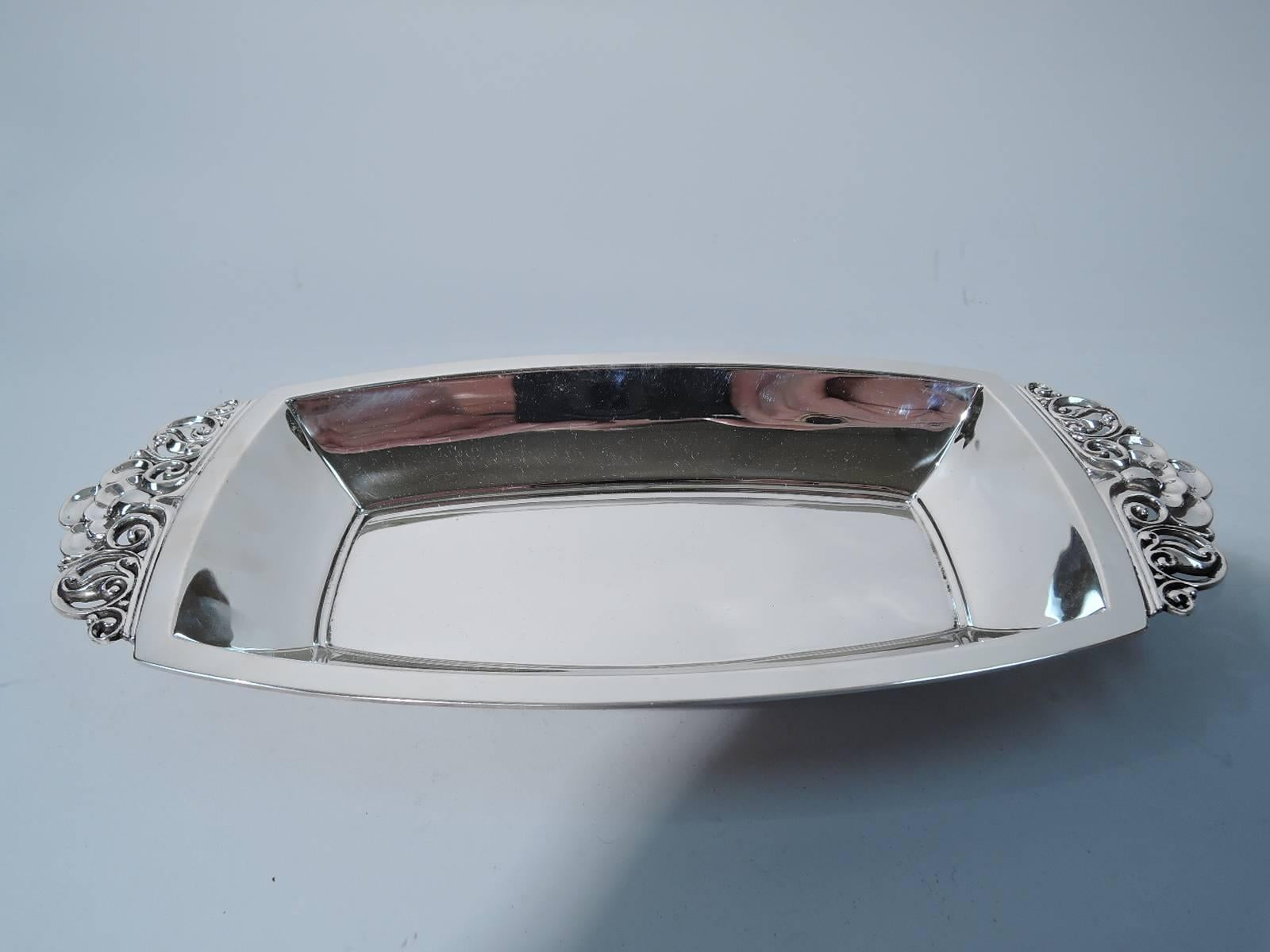 Sterling silver bread tray. Made by Tiffany & Co. in New York, circa 1950. Rectangular with curved sides and flat rim. Mounted to ends are handles with pierced stylized flowers and scrolls. Stark functionalism with the daring addition of ornament.