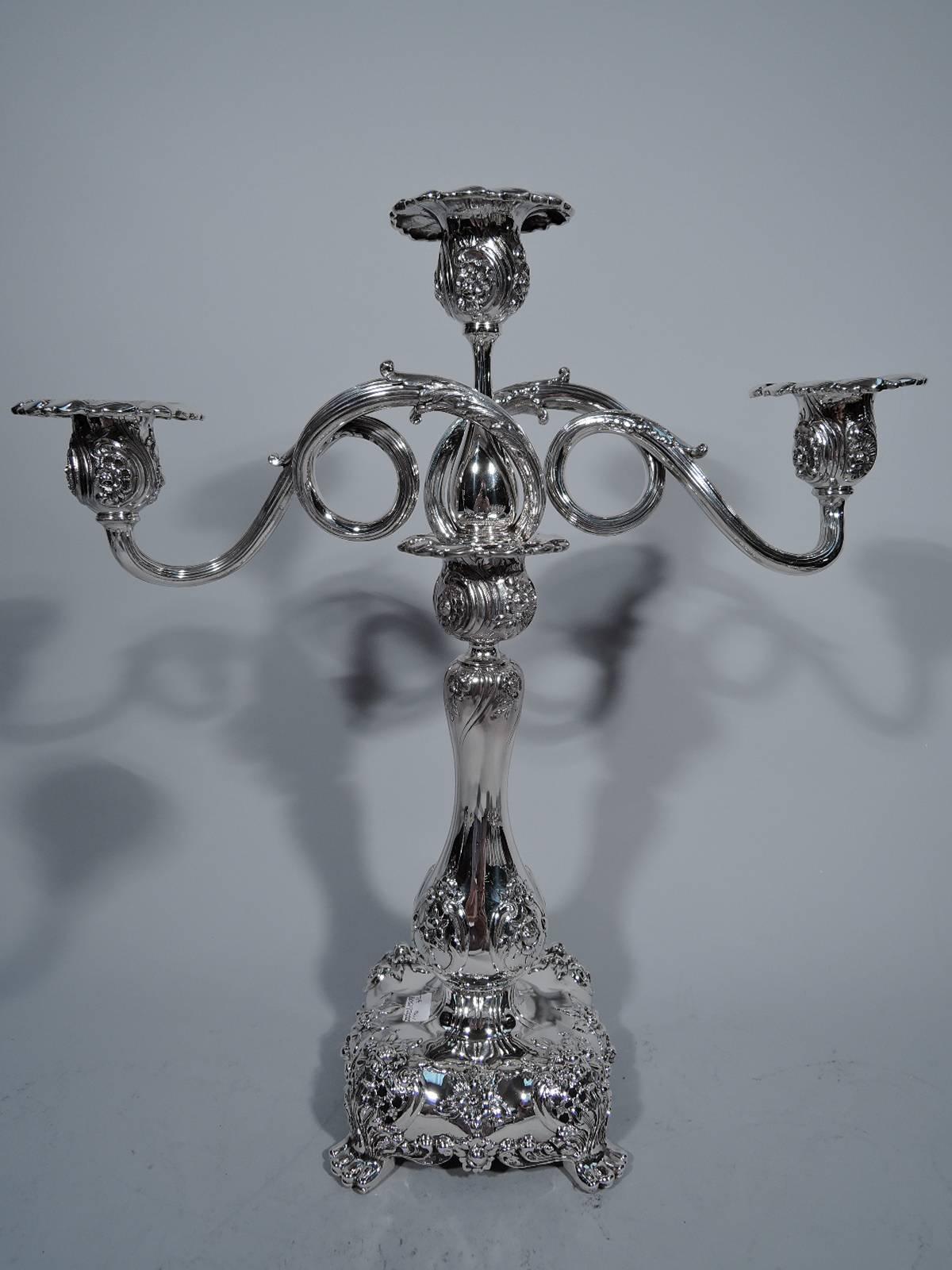 Pair of sterling silver three-light candelabra. Made by Tiffany & Co. in New York. Each: baluster shaft on squarish base with corner paw supports. Central light on baluster with wraparound and looping arms, each terminating in single light. Each arm