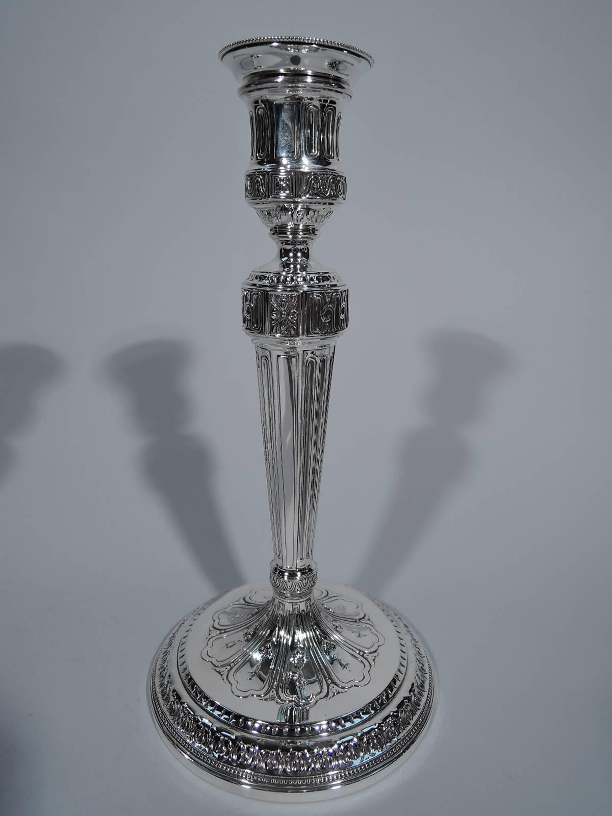 Pair of Neoclassical sterling silver candlesticks. Made by Tiffany & Co. in New York, ca 1914. Each: tapering columnar shaft on raised and stepped foot. Urn socket and detachable bobeche. Traditional ornament. Hallmark includes no. 18723 (first