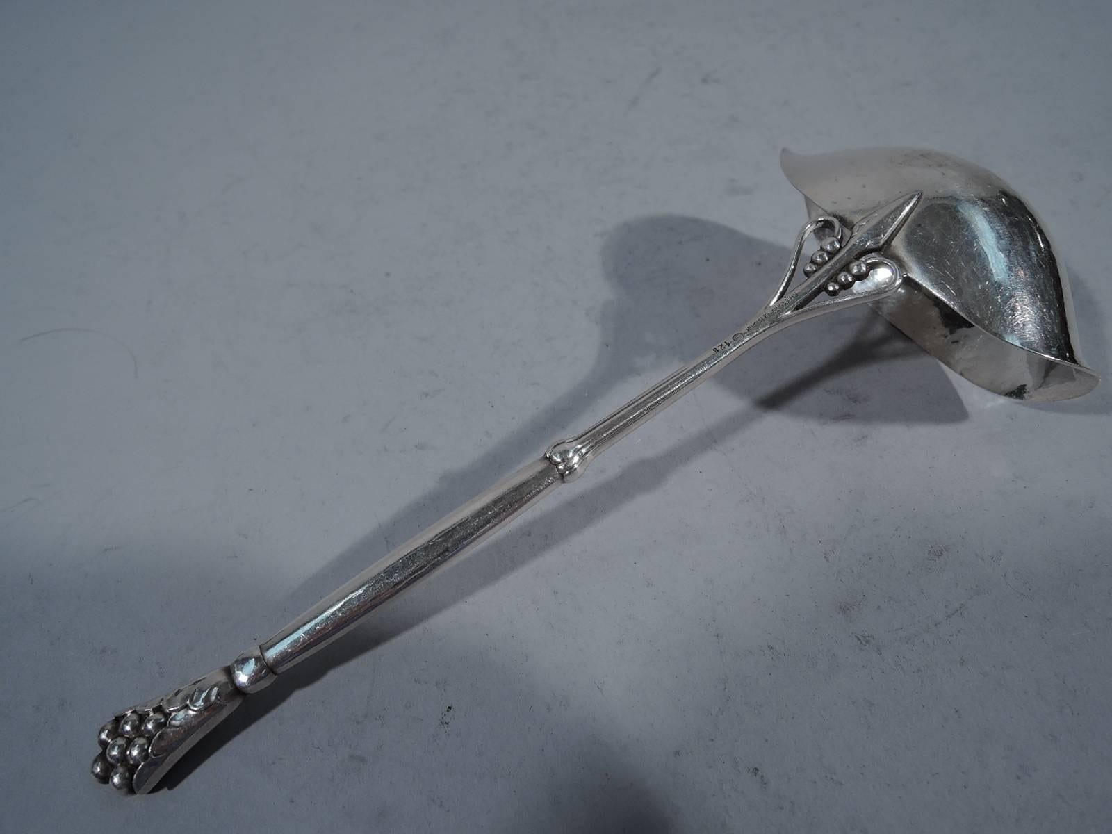 Sterling silver ladle in pattern no. 128. Made by Georg Jensen in Copenhagen. Bowl is “squashed” ovoid with two spouts and is mounted to handle with seeded scrolls. Handle terminal is leaf-wrapped berry. Visible hand hammering. This model is