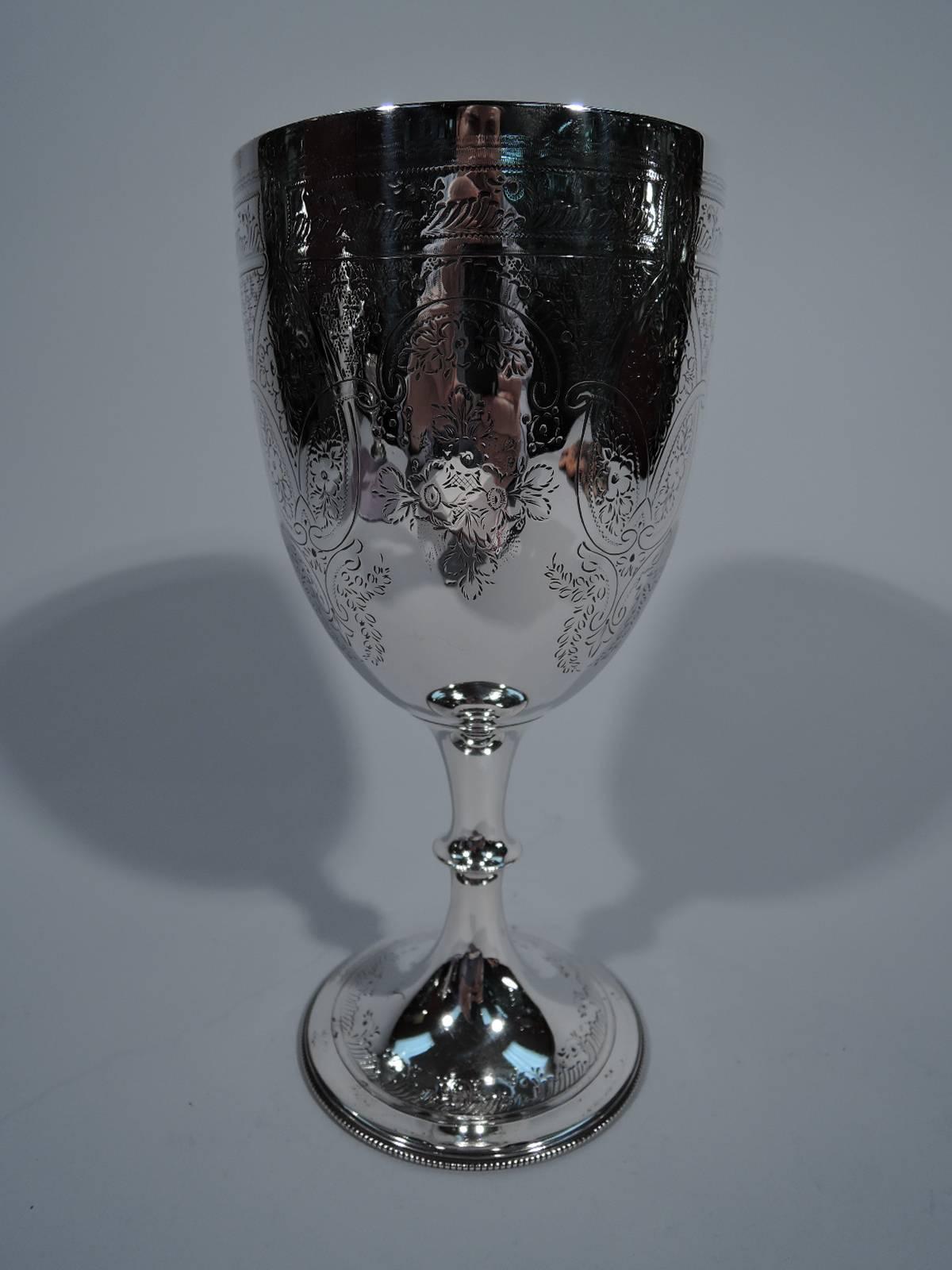 Edwardian sterling silver goblet. Made by Walker & Hall in Sheffield in 1902. Tall bowl with curved base mounted to stem with flange knop on raised foot. Knop has dentil rim. Foot has beaded rim. Engraved scrolled border comprising C-scrolls, and