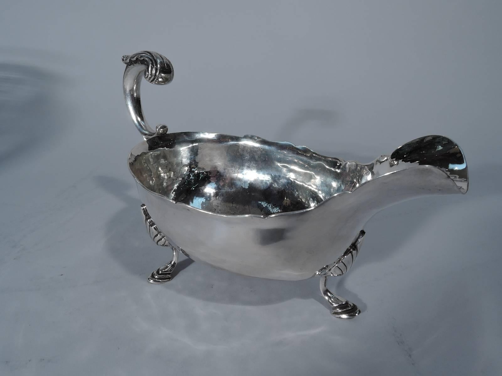 Sterling silver gravy boat. Made by William G. DeMatteo in Bergenfield, New Jersey, ca 1950. Ovoid and curved body with scrolled rim, wide lip spout, double-scroll flying handle with leaf cap and three hoof supports with shell mounts. Visible hand