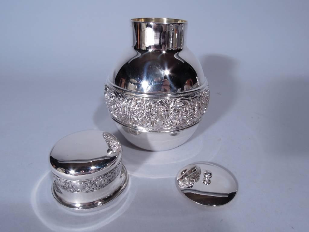 Sterling silver tea caddy. Made by Tiffany & Co. in New York. Globular with applied repousse band of scrolls and flowers on stippled ground. Interior cap with ball finial set in short neck. Cover has same ornamental band and flared and molded rim.