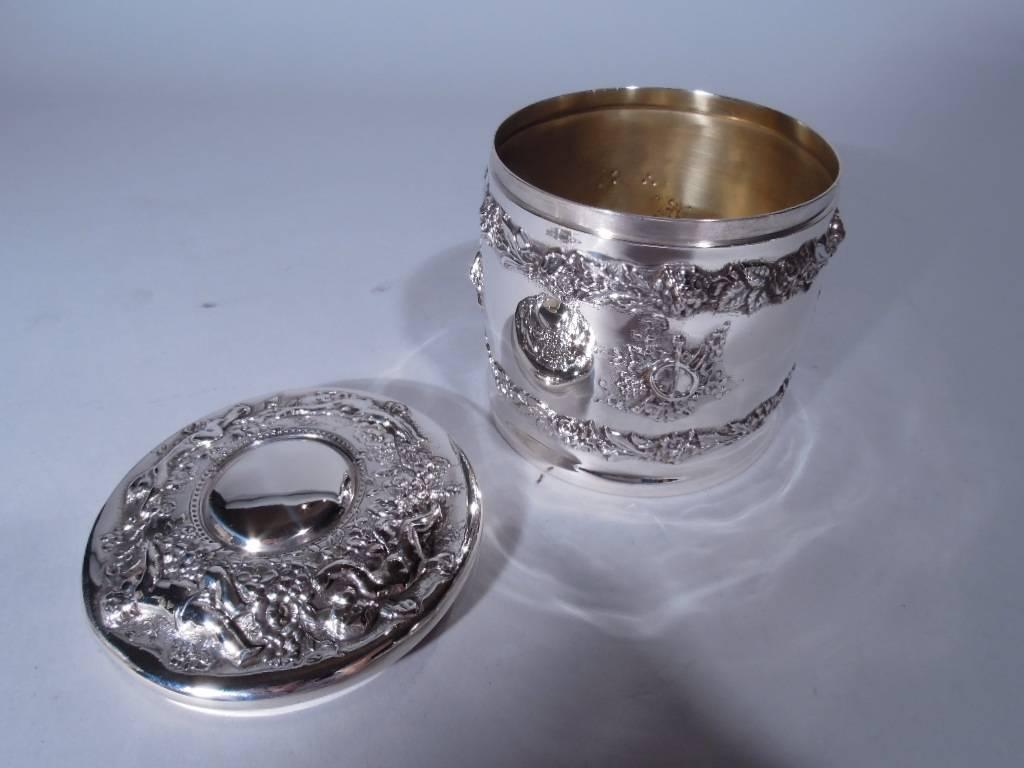 Rococo sterling silver trinket box. Made by Tiffany & Co. in New York. Drum-form with gently curved sides and cover. Applied floral garlands and art trophies, and repousse chubby cherubs. A tactile interpretation of 18th century French design.