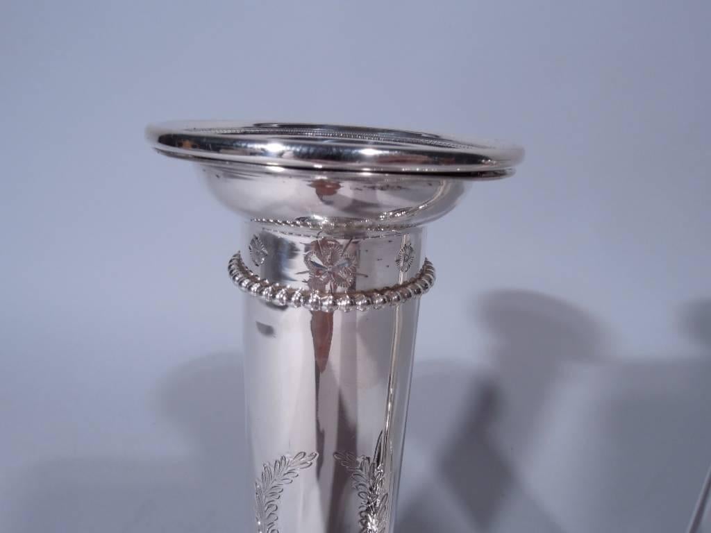 Pair of sterling silver candlesticks. Made by Goodnow & Jenks in Boston, circa 1900. Each: columnar shaft mounted to raised foot. Detachable bobeche with leaf-and-dart border. Beading to column top and foot. Engraved wreath (vacant). Hallmark