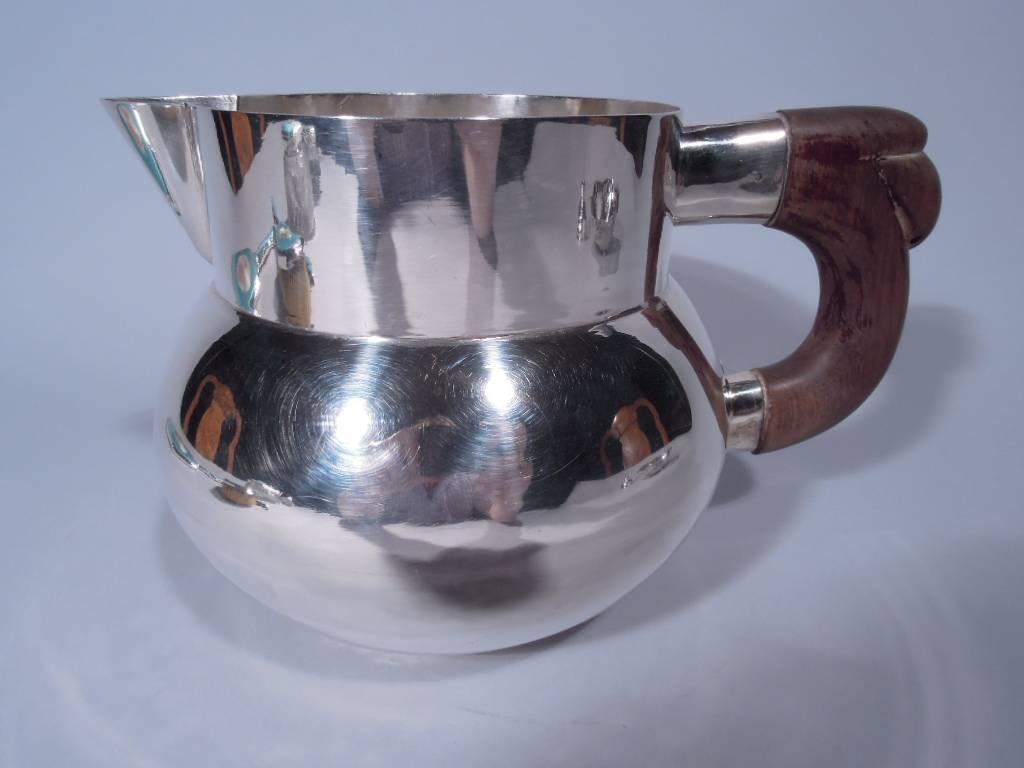Beautiful and spare sterling silver water. Bulbous body with short straight neck and V-spout. Carved wood handle is c-scroll with abstract leaf cap. Handmade with hammer blows visible inside. Hallmarked “Anton-Plata 925-Mexico.” Nice condition and