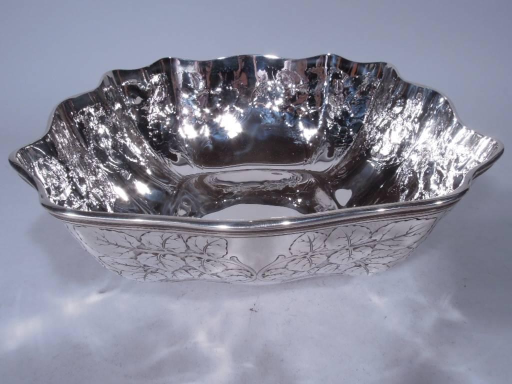Edwardian sterling silver bowl. Made by Tiffany & Co. in New York, circa 1907. Four wavy sides with molded rim. Acid-etched ornament on exterior: on each side scrolled leafy branches form a shaped frame (vacant). Corners concave with intertwined