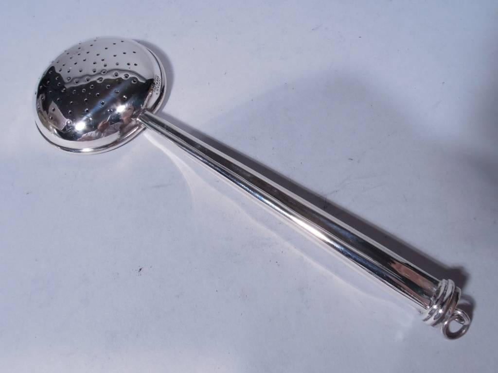 Sterling silver tea strainer. Retailed by Tiffany & Co. in New York. Fluted and tapering handle with stepped terminal and loose-mounted ring. Bowl round and shallow with pierced star. Hallmarked “Tiffany Sterling Portugal”. Nice