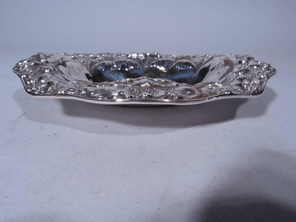 Art Nouveau sterling silver bowl. Made by Gorham in Providence, circa 1890. Plain oval well with scalloped sides and wavy scrolled rim. Rim has dense and tactile repousse decoration: flowers on whiplash stems and lush and ripe blooms. Script