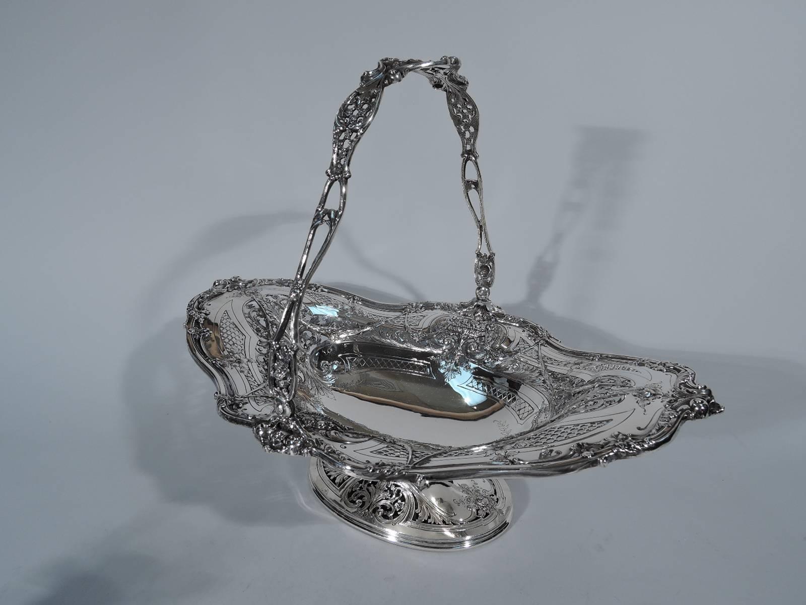 Fancy sterling silver basket. Made by Black, Starr & Frost in New York, circa 1885. Oval well with flared and asymmetrical rim, raised oval foot, and swing handle. Flowers, foliage, swags, and scrolls – the works. Lavish turn-of-the-century fashion.