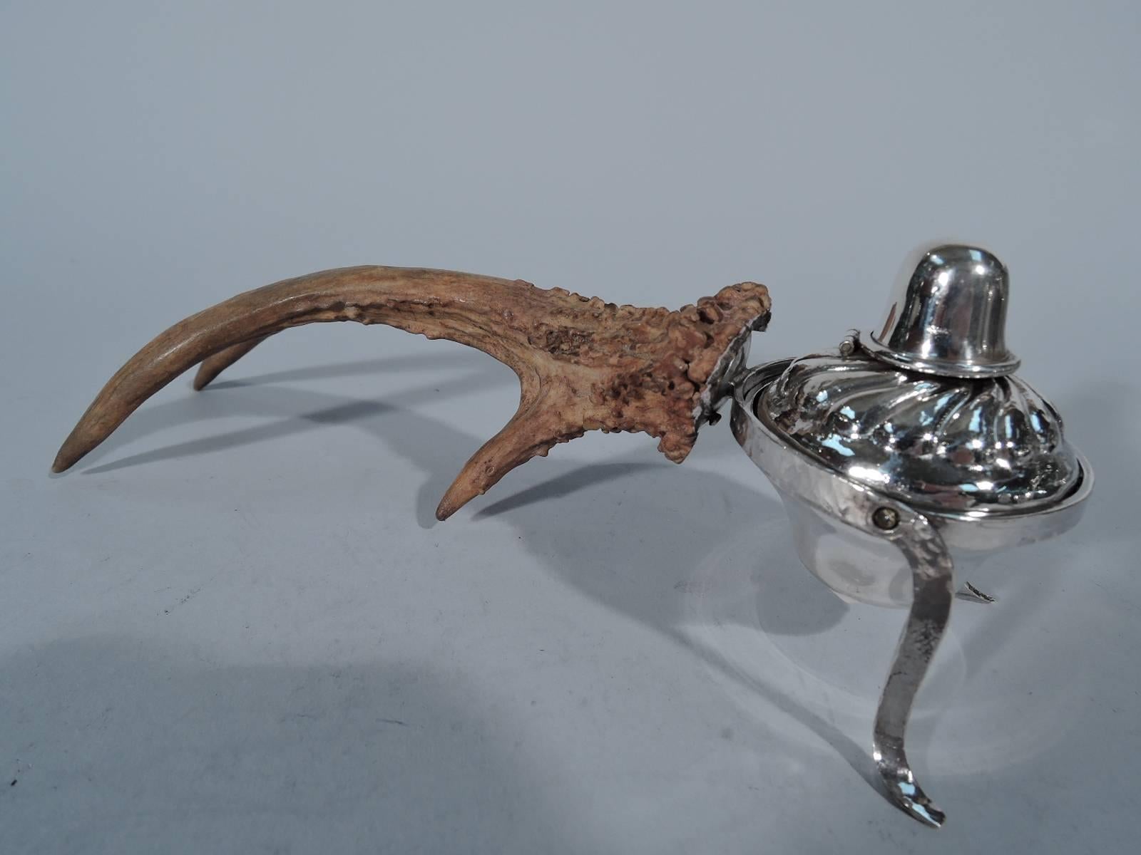 American sterling silver cigar lighter mounted to antler support, circa 1900. The lighter has a gadrooned top and hinged cover and is swing-mounted to hand-hammered C-frame with L-form supports. The frame in turn is mounted to a corrugated and