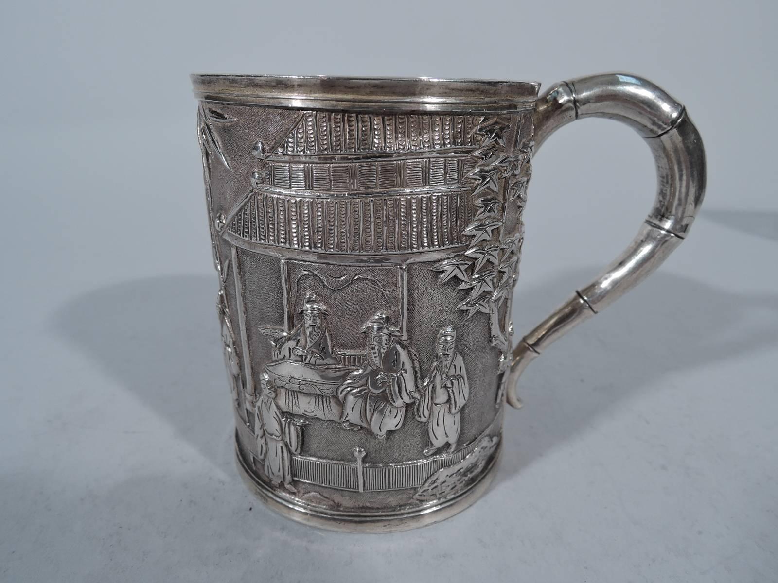 Chinese export silver mug, circa 1890. Straight sides with chased and repousse scenes of daily life, including robed greybeards, pavilions and bamboo. A sweet deployment of exotic motifs. The scrolled bamboo handle completes the look. Armorial frame