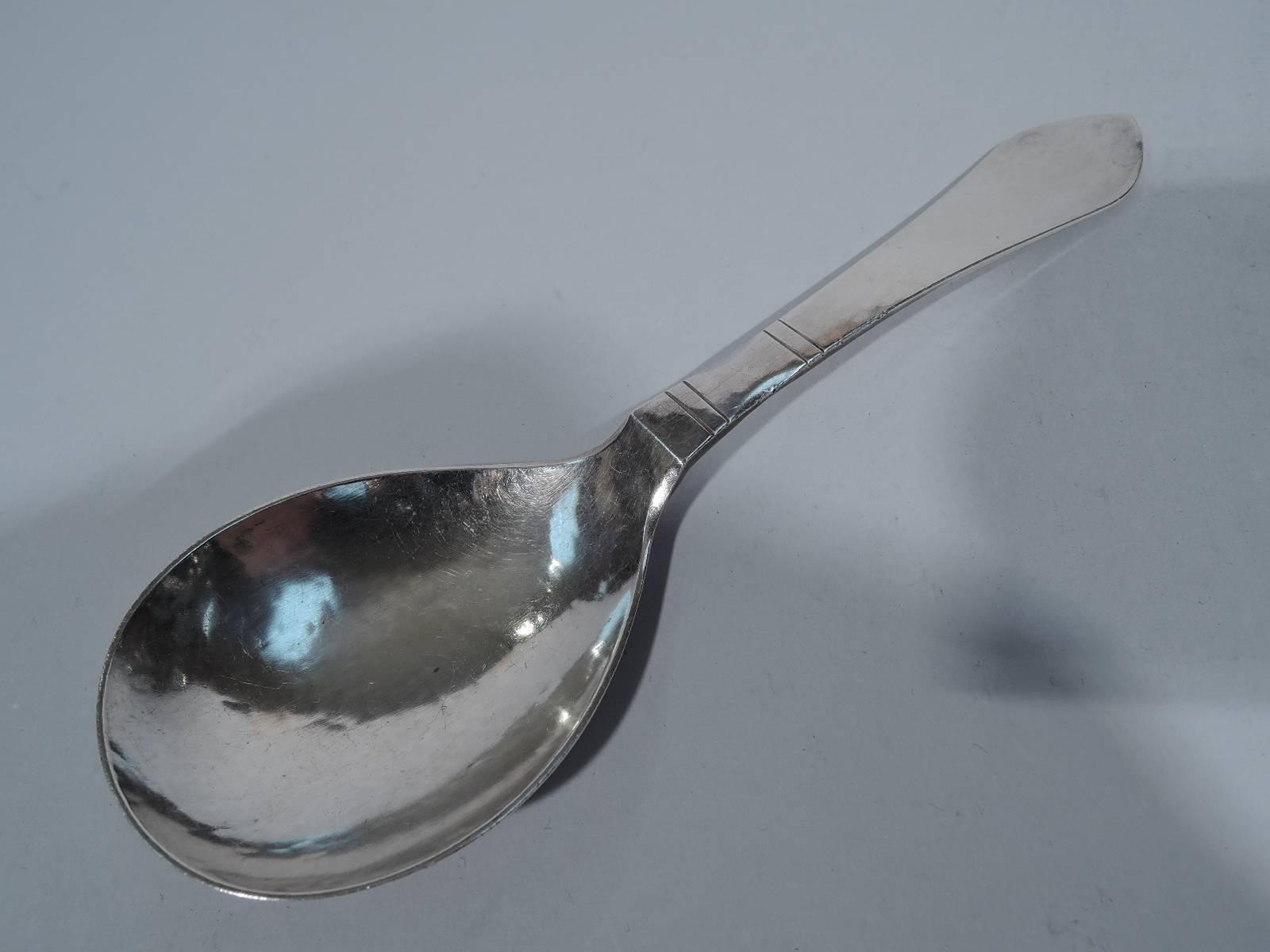 Hand-hammered sterling silver serving spoon in continental pattern. Made by Georg Jensen in Copenhagen. Shallow oval bowl and pointed terminal. Spare ornament in the form of incised horizontal bands. An early piece in this early pattern, which was