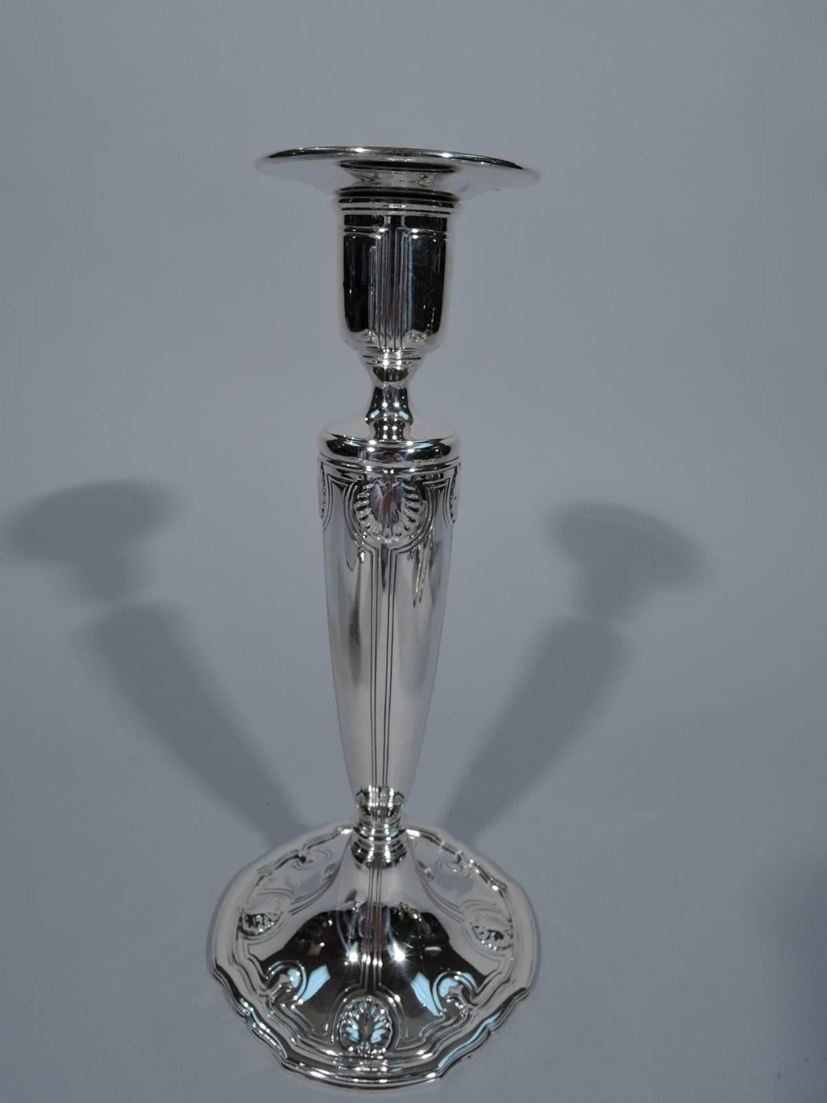 Pair of sterling silver candlesticks. Made by Tiffany & Co. in New York, circa 1911. Each: Tapering column on shaped foot, urn socket and detachable bobeche. Engraved curvilinear frames and applied scallop shells and trefoils. Restrained and soft.