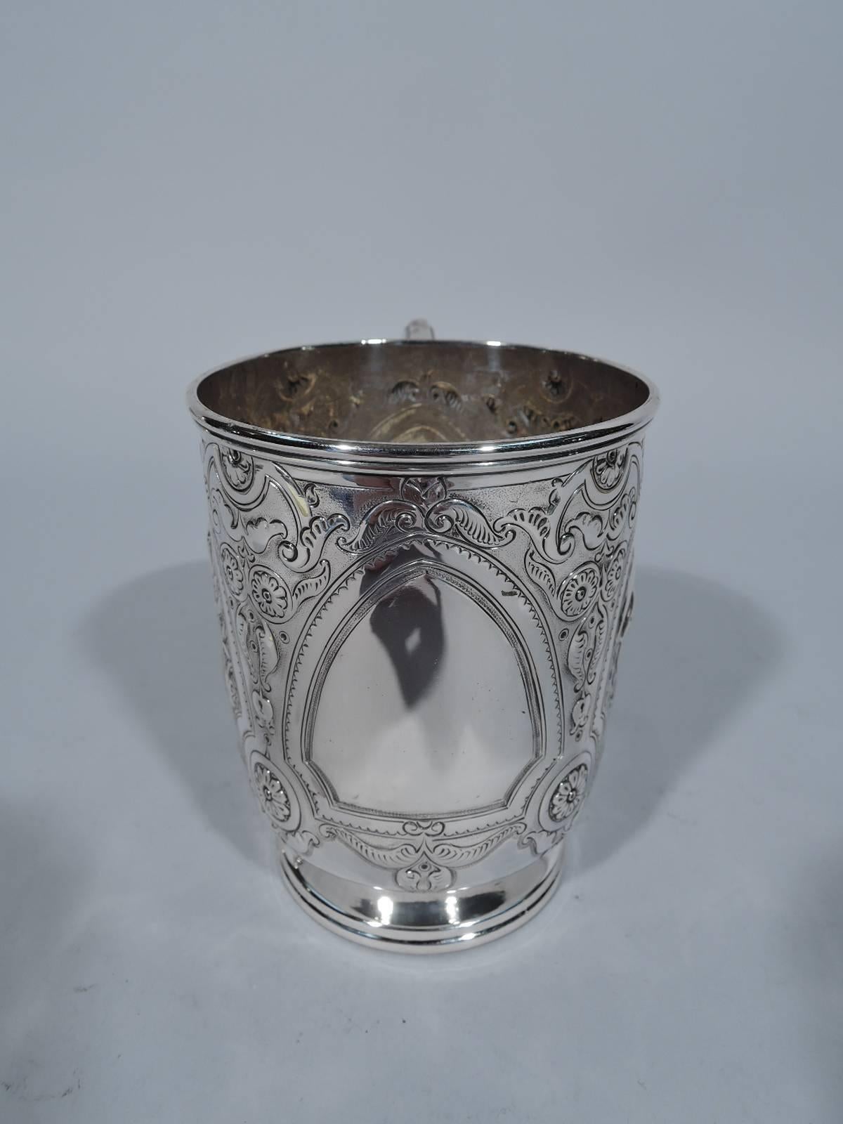 Victorian sterling silver christening mug. Made by Thomas Bradbury & J. Henderson in London in 1880. Stepped foot, scrolled bracket handle, and molded rim. Flowers, foliage, and scrolls surrounding curved and scalloped triangular frames inset with