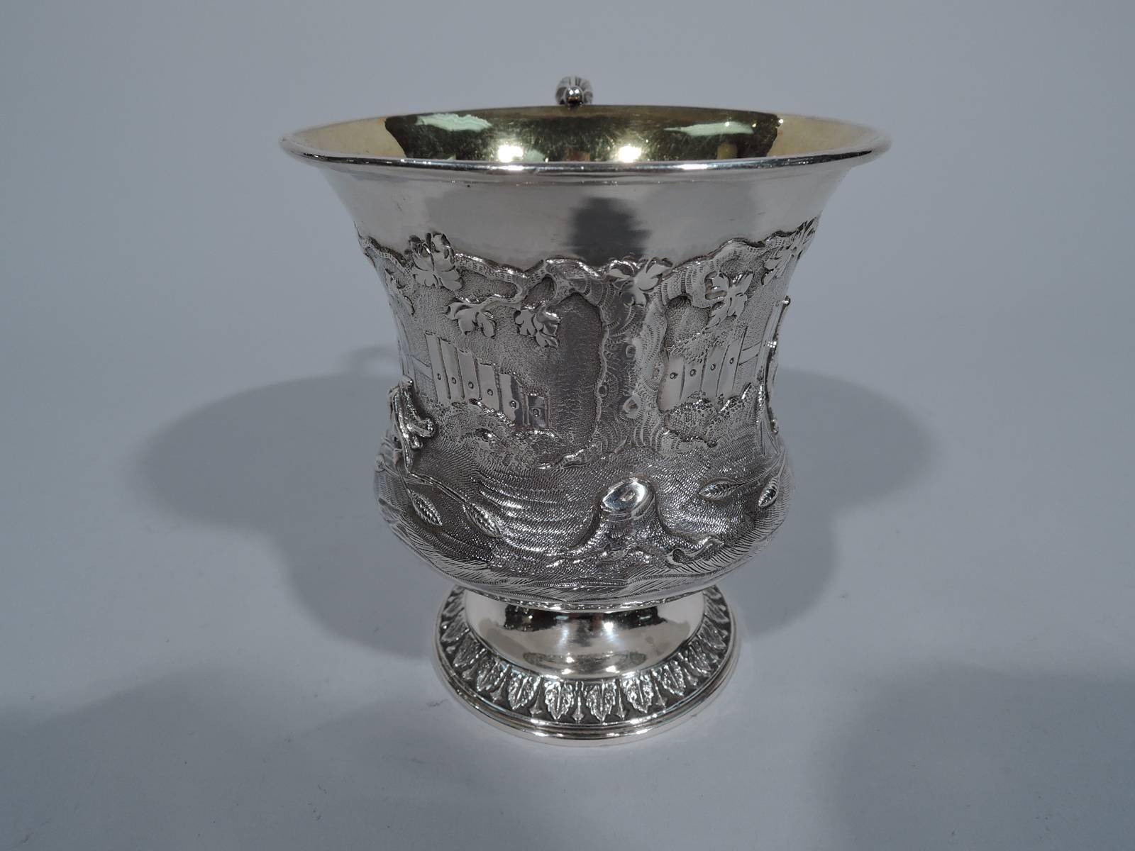 George IV sterling silver christening mug. Made in London in 1829. Baluster body with flared rim, leaf-capped s-scroll handle and raised foot. Repousse scene with fowl waddling in a fenced yard. Foot has chased leaf-and-dart border. Richly gilt