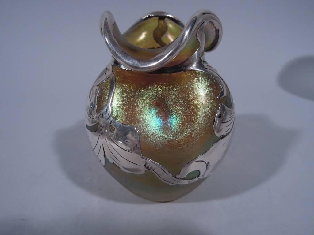 American iridescent glass bud vase with silver overlay. Baluster with pinched shoulders and asymmetrical wavy rim. Semi-abstract leaves heightened with engraving laid over shimmering greenish-gold glass. Unmarked. Nice color and