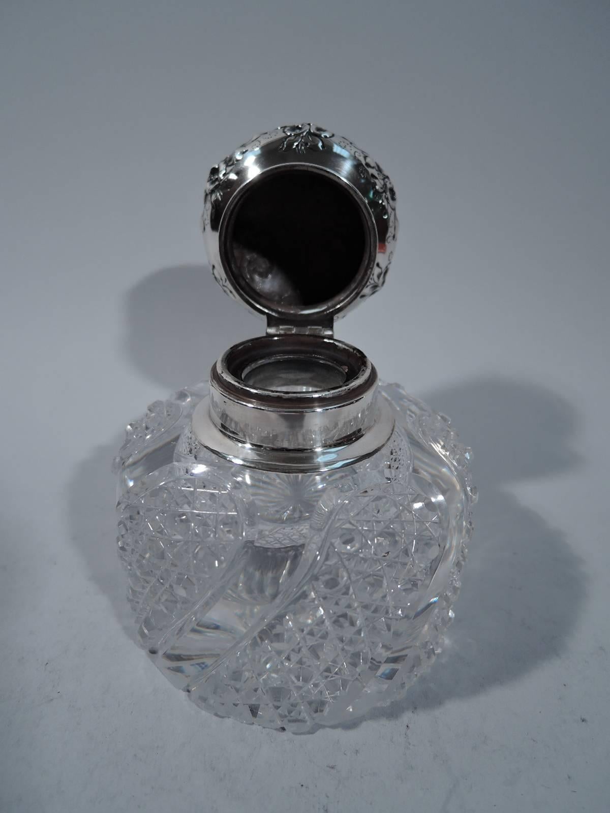 Sterling silver and cut-glass inkwell. Made by Shiebler in New York, circa 1890. Drum-form with brilliant-cut twisted lobes. Short neck in silver collar with hinged bun cover. Cover has repousse flowers and bow-tied ribbons. Center vacant. Hallmark