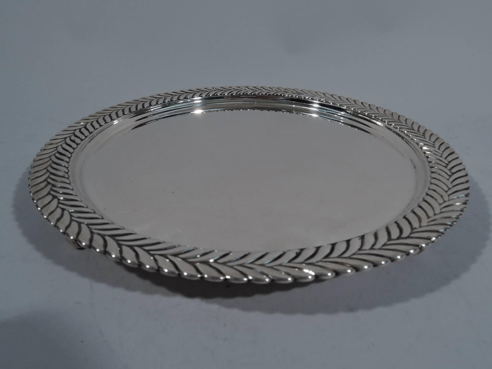 Sterling silver salver. Made by Tiffany & Co. in New York. Circular with plain well. Rim has semi-abstract imbricated leaf ornament. Bold Georgian inspiration. Rests on three traditional volute scrolls with same mount. Hallmark includes pattern no.