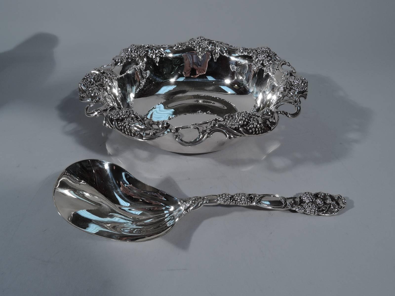 Sterling silver berry bowl with spoon. Made by Tiffany & Co. in New York, circa 1905. Bowl: Round with gently curved sides. Turned-down and pierced rim has bunches of succulent berries alternating with open scrolls. Spoon: Same motif with flower