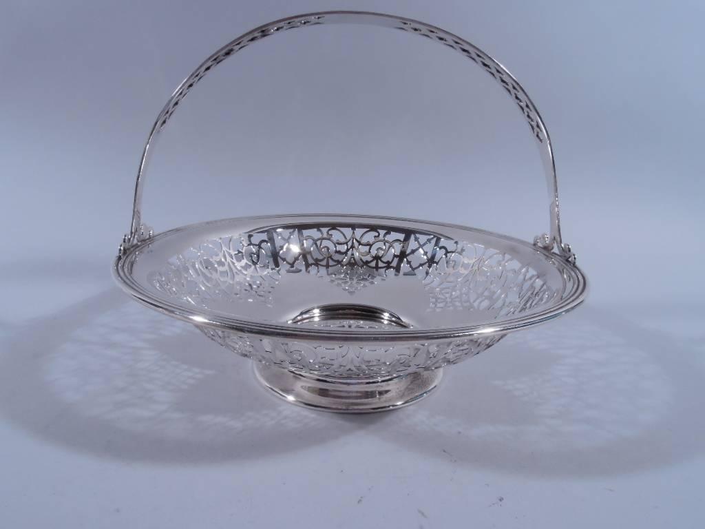 Edwardian sterling silver basket. Made by Gorham in Providence in 1915. Shallow curved bowl with solid petal well and pierced ornament. Stationary C-scroll handle has pierced quatrefoils and trefoils and solid center. Reeded rim and raised foot.