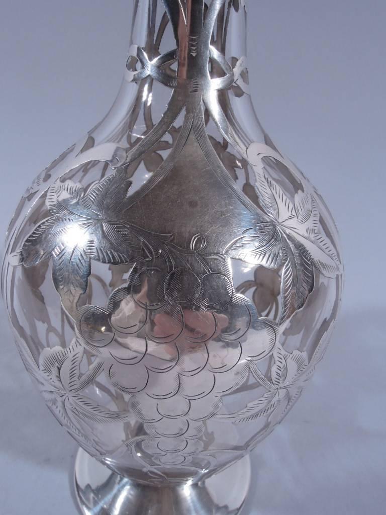 American handblown clear glass decanter and stopper with silver overlay, circa 1900. Baluster body neck, everted rim, and flat foot. Ball stopper with conical finial, spool neck, and short plug. Silver overlay in form of fruiting grapevine. Pontil