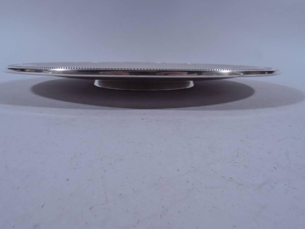 Spare and modern sterling silver footed plate. Made by Tiffany & Co. in New York. Shallow with inset rim beading and incised central well. Short and spread foot. Hallmark includes postwar pattern no. 23672. Very good condition.

Dimensions: H 1 x